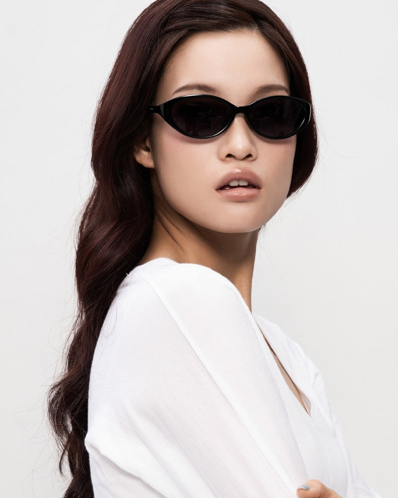 A model in SEEYAA! black oval sunglasses, arms crossed, looking back at the camera.