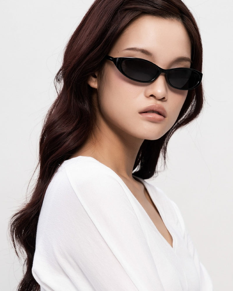 A model in SEEYAA! slim black sunglasses, head turned to the side.